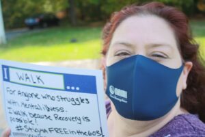 Woman in a mask holding an I Walk sign for NAMIWalks NH