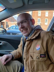 Smiling man in a brown jacket with an I Voted Today sticker