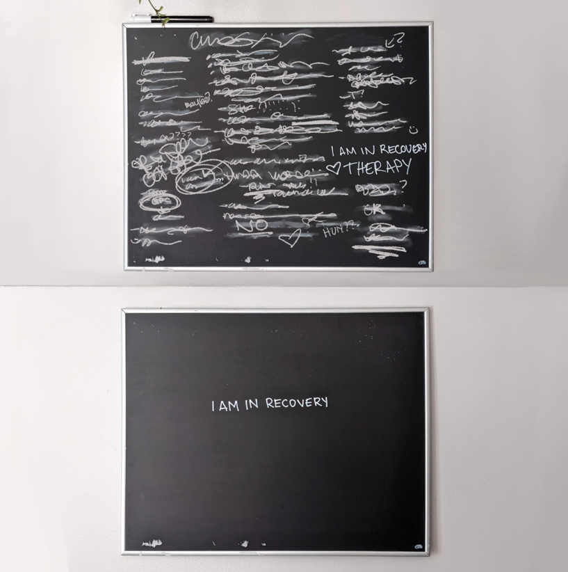 Two chalkboards are stacked on top of one another. The top chalkboard feathers many words crossed out with, "I am in Recovery Therapy" legible. The second chalkboard has only "I am in Recovery" written in the middle.