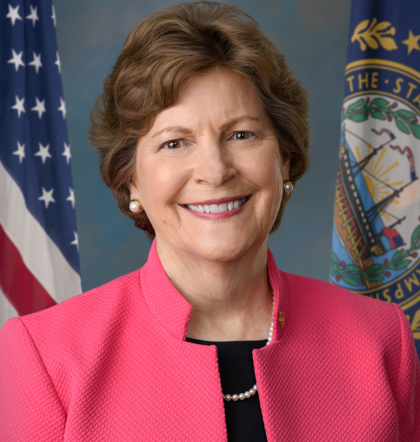 Woman in a pink jacket with an American flag and a New Hampshire state flag in the background